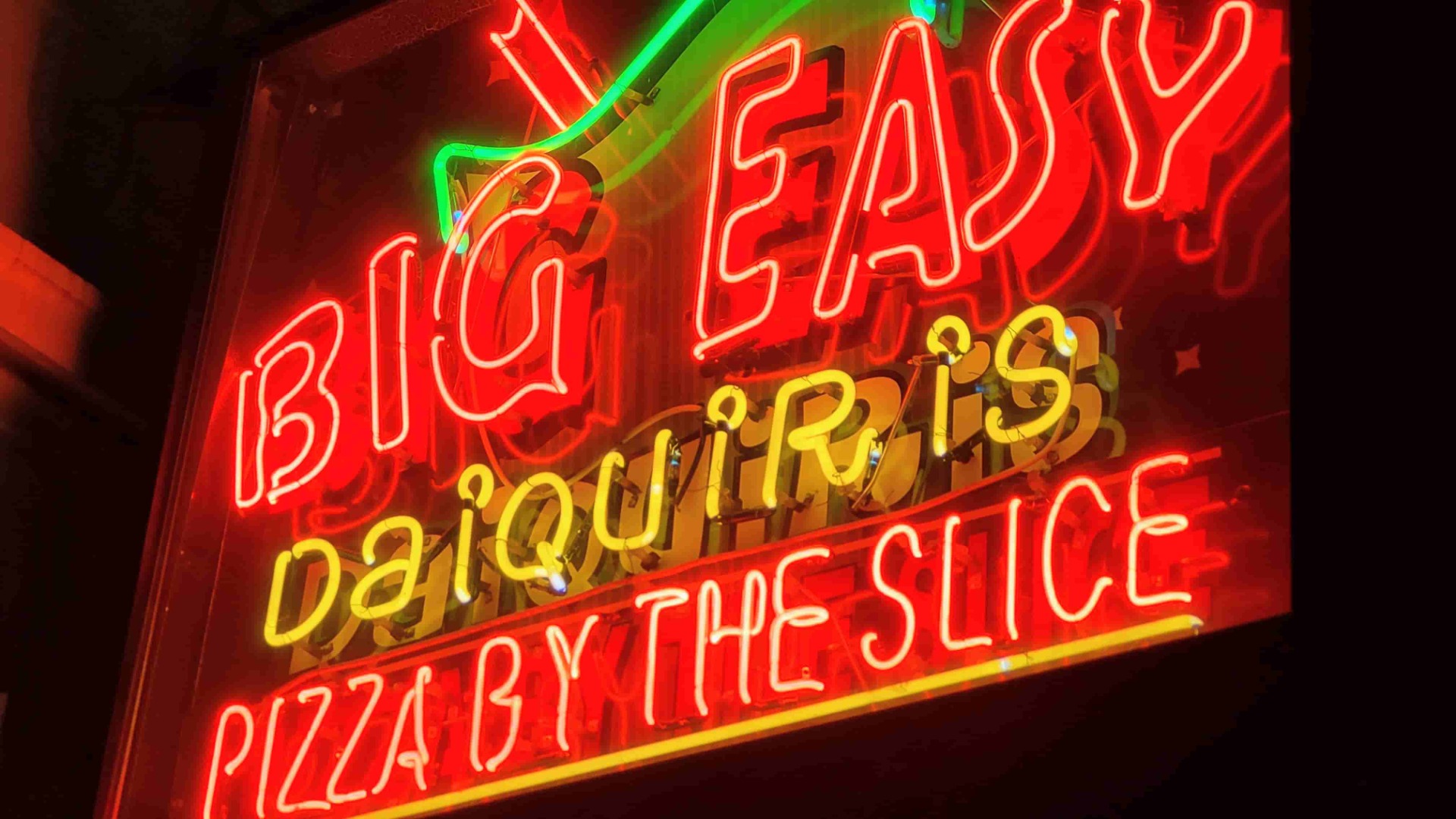 Neon-Schriftzug in Rot, Grün und Gelb an einer Wand, mit leuchtenden Zahlen und Linien.